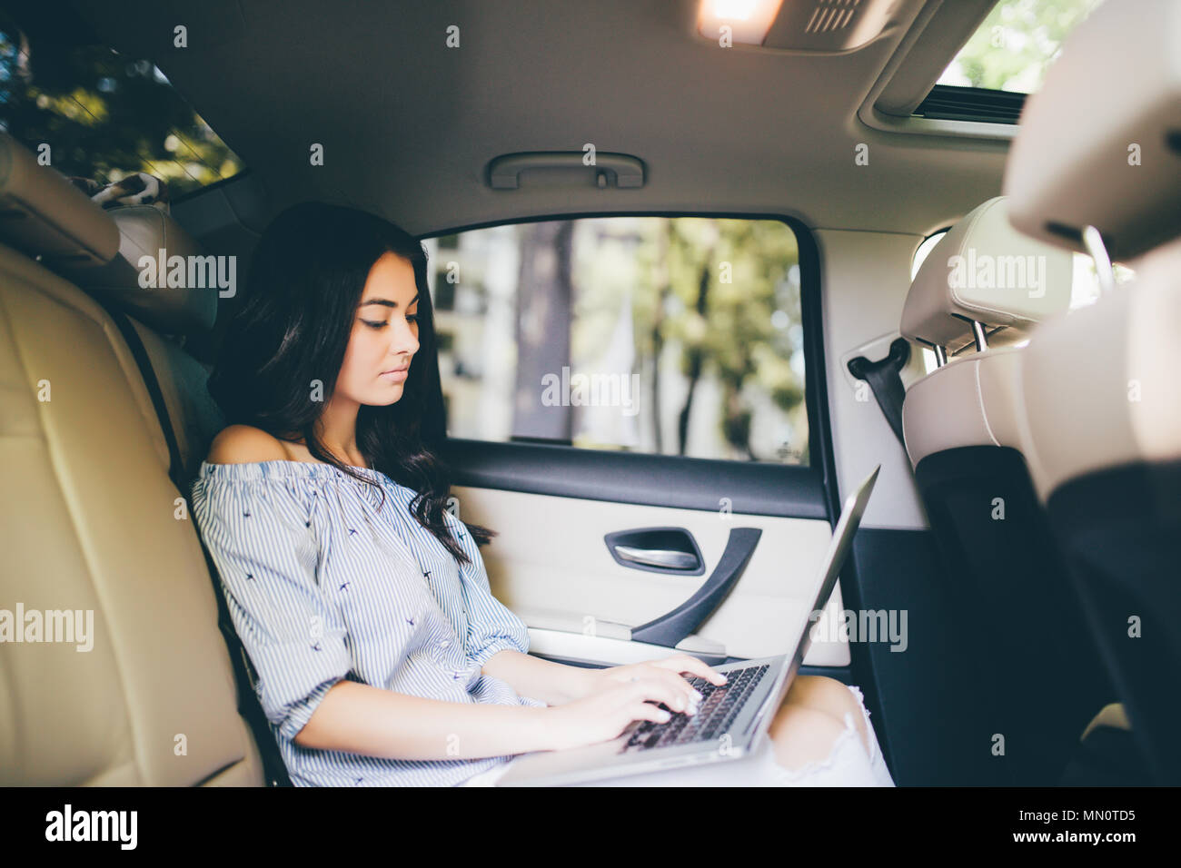 Bella donna d'affari sta usando un computer portatile mentre è seduto sul sedile posteriore in auto Foto Stock
