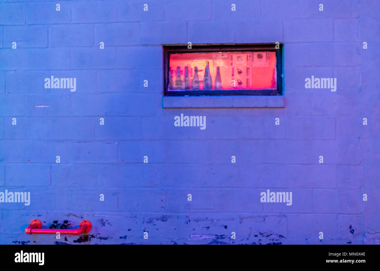 Immagine scattata di notte di una piccola finestra rettangolare, incandescente arancione in un blocco in calcestruzzo parete in Portland Maine Foto Stock