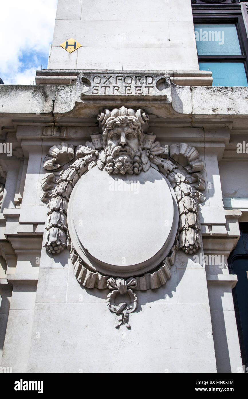 Frame ovale circondato da ghirlande di fiori e nastri con una scultura di testa che decorano la facciata di dal grande magazzino Selfridges, London, Regno Unito Foto Stock