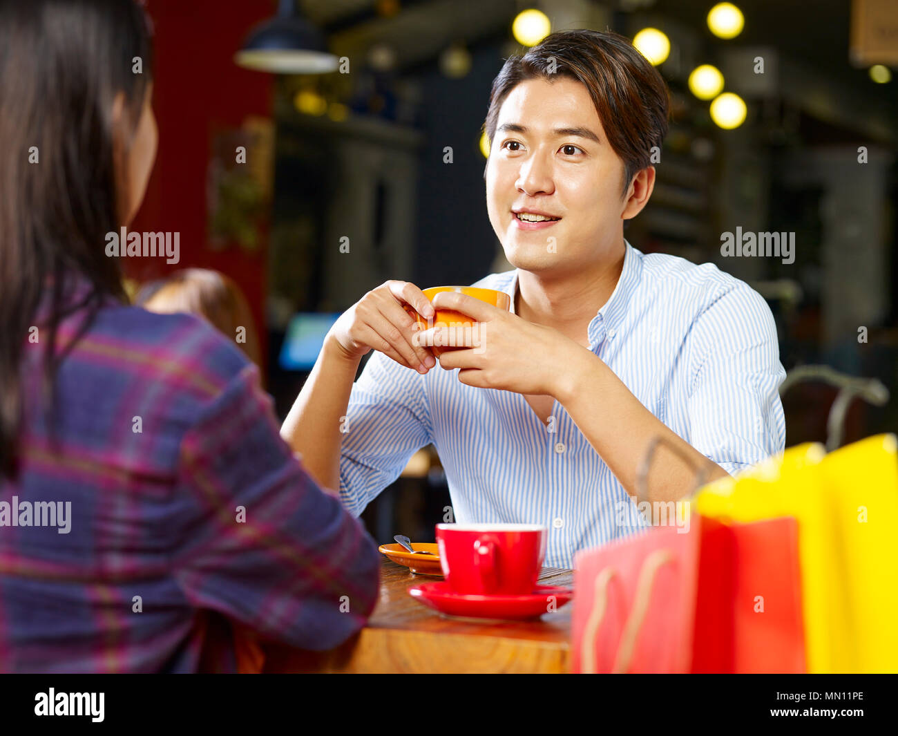 Giovani asiatici gli amanti della coppia seduta a tavola in chat parlando in coffee shop dopo lo shopping. Foto Stock