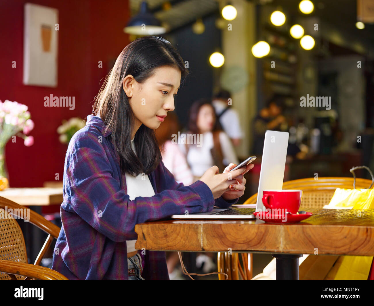 Giovane donna asiatica in seduta coffee shop mediante telefono cellulare e computer portatile. Foto Stock