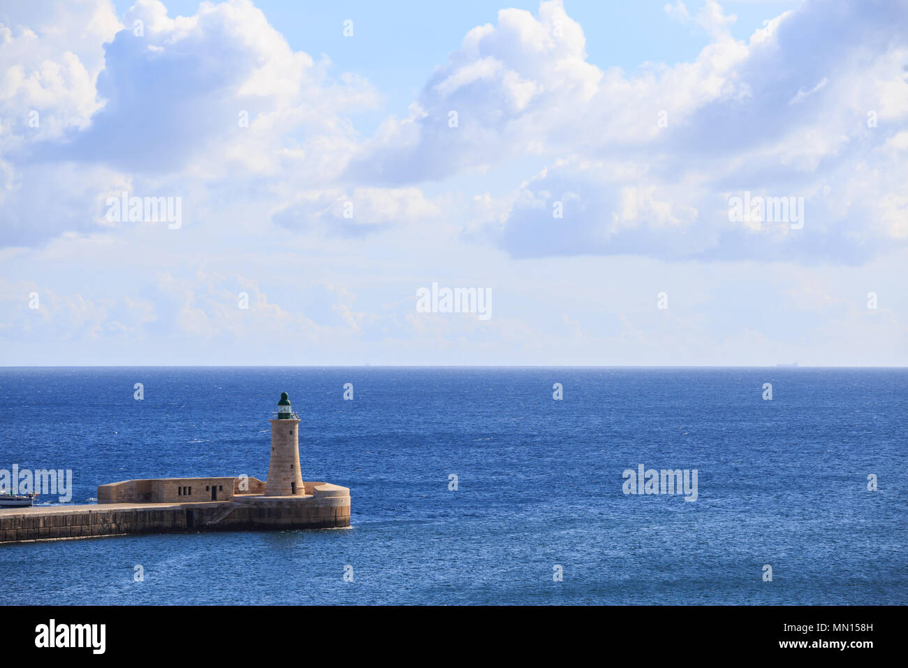 San Elmo faro a La Valletta, Malta. Struttura di frangionde del Grand Harbour tra il blu del mare e cielo nuvoloso sfondo. Foto Stock