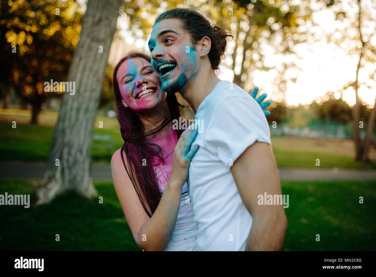 Sorridente giovane coppia con polvere colorata cosparso sui loro volti. Allegro l uomo e la donna godendo festival dei colori esterni al parco. Foto Stock