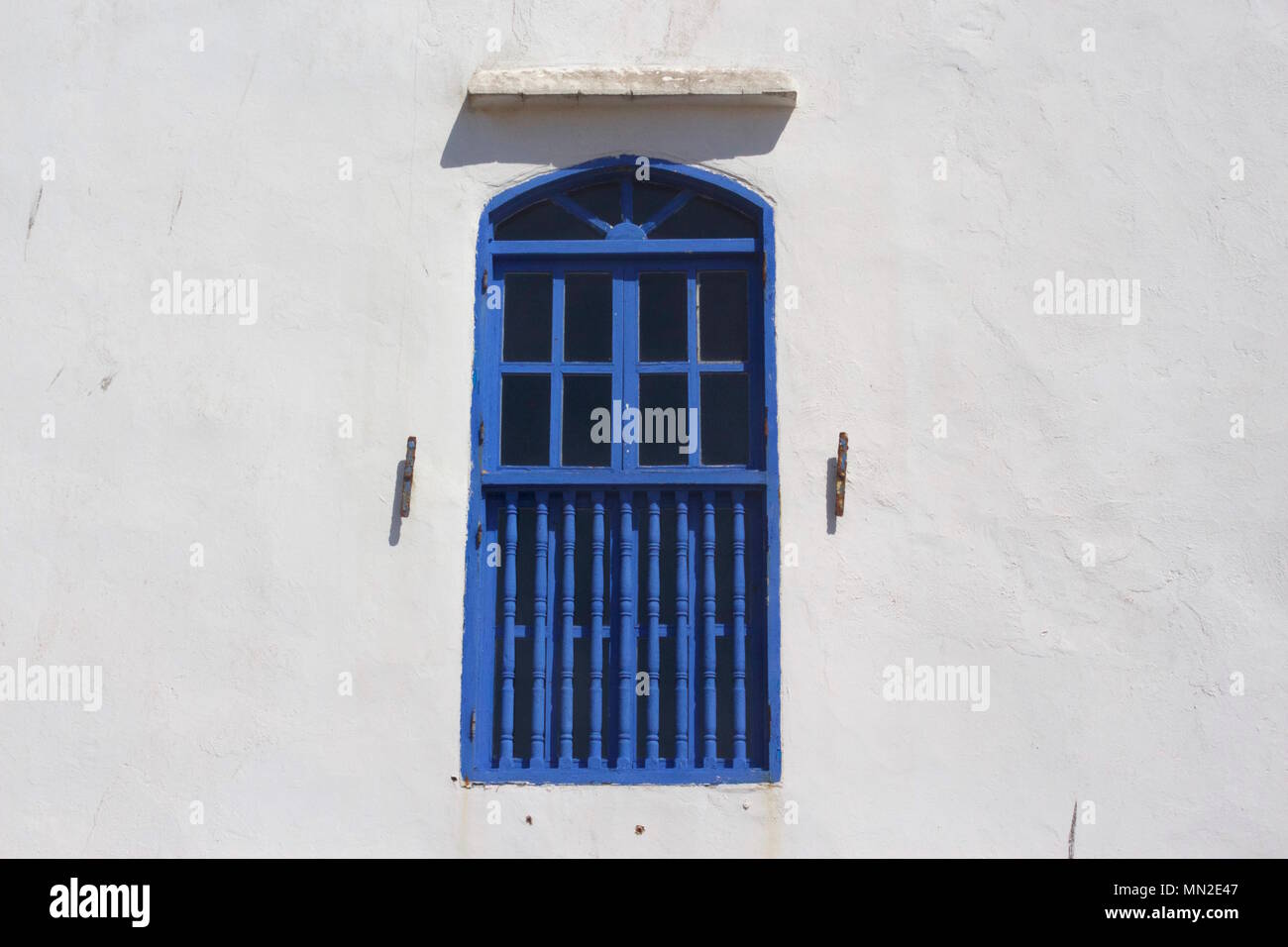 Finestra blu contro un muro bianco a Essaouira, Marocco Foto Stock