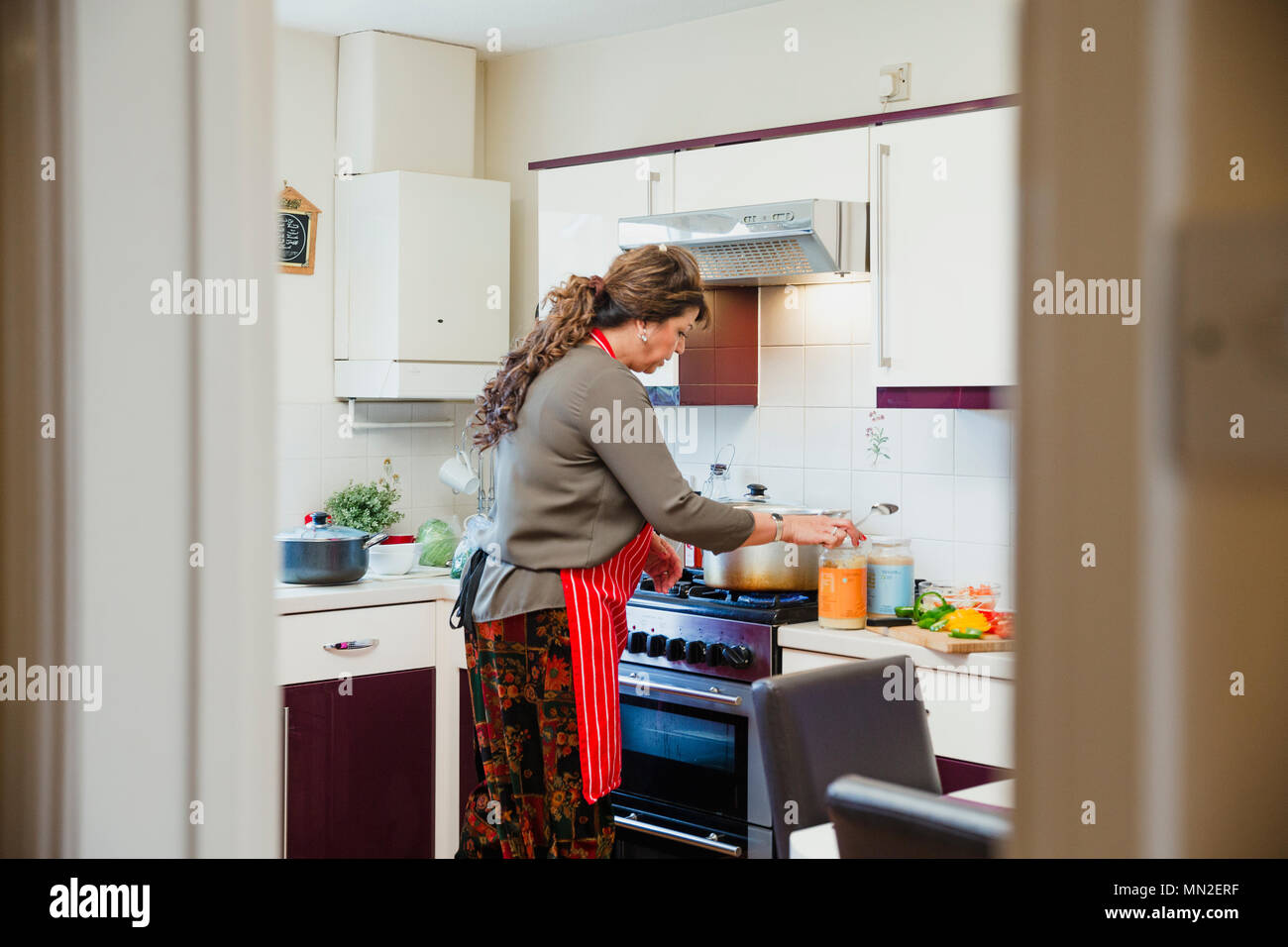 Donna matura è in piedi presso il fornello nella cucina di casa sua, la preparazione di ingredienti per un curry. Foto Stock