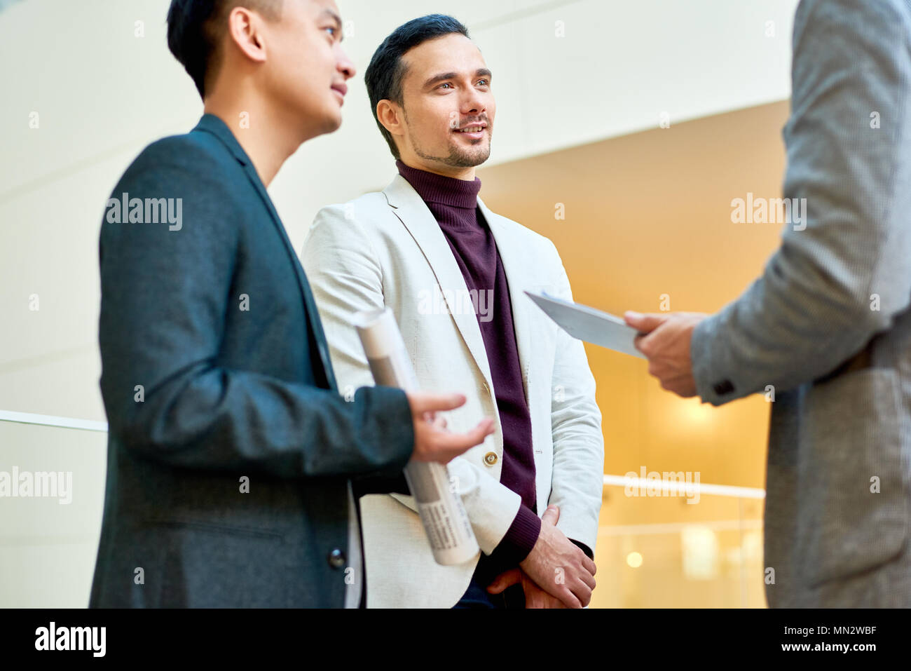 Ritratto di imprenditore bello discutere di un progetto di collaborazione con i colleghi in piedi nella hall di un ufficio moderno edificio, spazio di copia Foto Stock