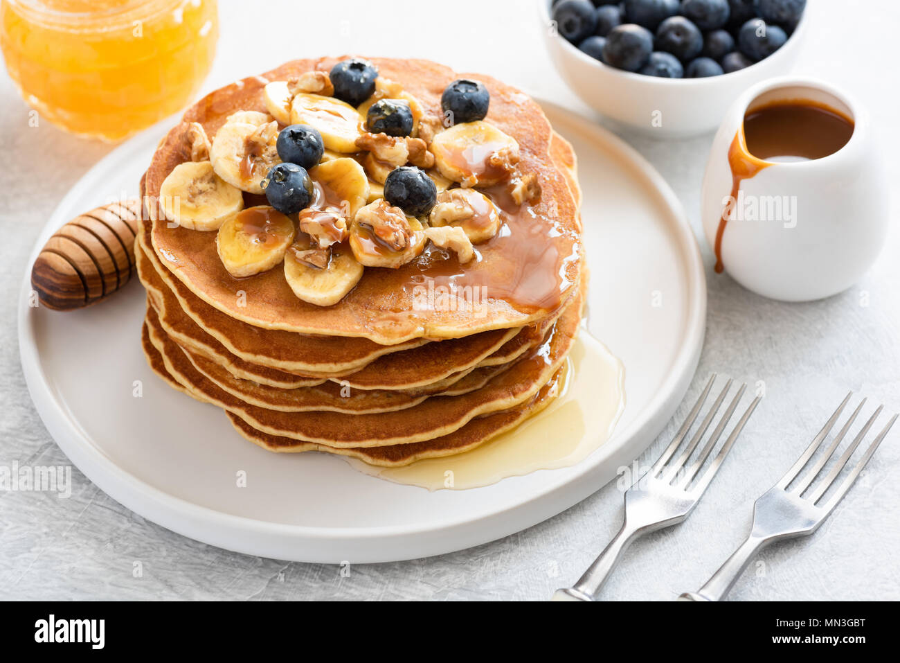 Pila di frittelle di banane, mirtilli, noci, miele e salsa di caramello sulla piastra bianca. Primo piano. La colazione pancake con sciroppo d'acero Foto Stock