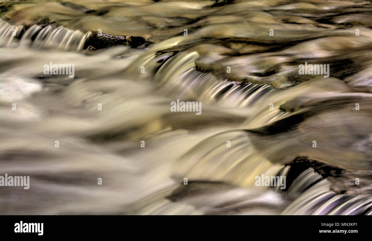 Un primo piano di una piccola cascata che mostra tutti gli intricati movimento dell'acqua che cade e volute sulle rocce in streambed. Elaborati come un Foto Stock