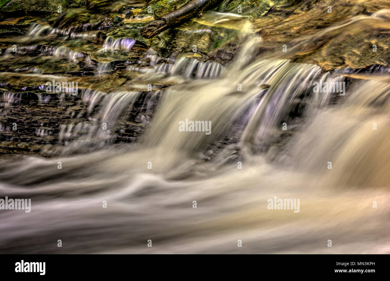 Un primo piano di una piccola cascata che mostra tutti gli intricati movimento dell'acqua che cade e volute sulle rocce in streambed. Elaborati come un Foto Stock