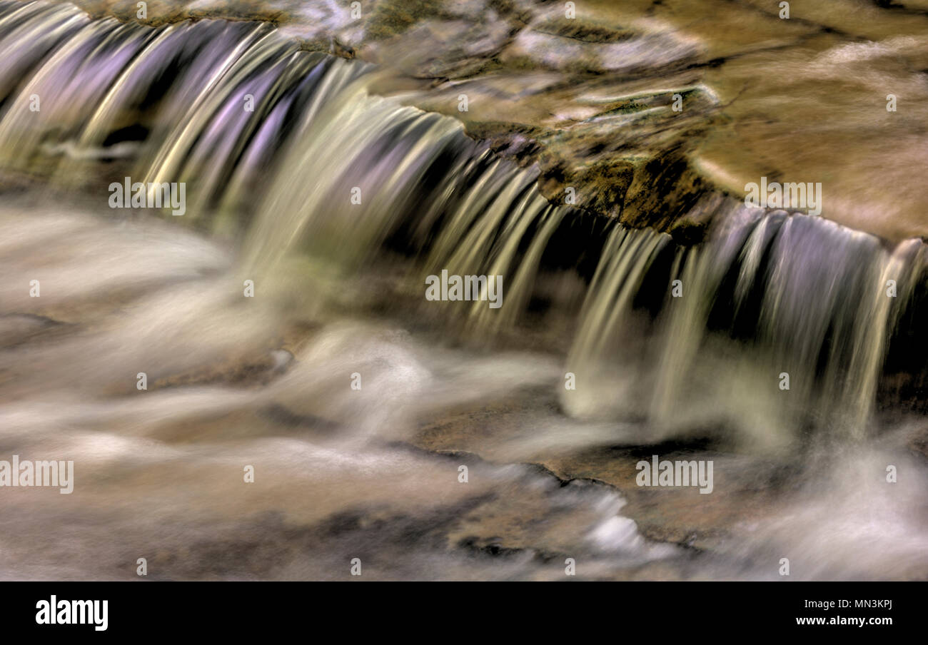 Un primo piano di una piccola cascata che mostra tutti gli intricati movimento dell'acqua che cade e volute sulle rocce in streambed. Elaborati come un Foto Stock