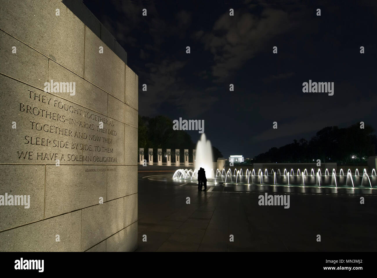 Il Memoriale della Seconda Guerra Mondiale durante la notte. Un paio di pagare i loro aspetti si stagliano nella fontana. L'iscrizione sulla parete può essere letto. Foto Stock