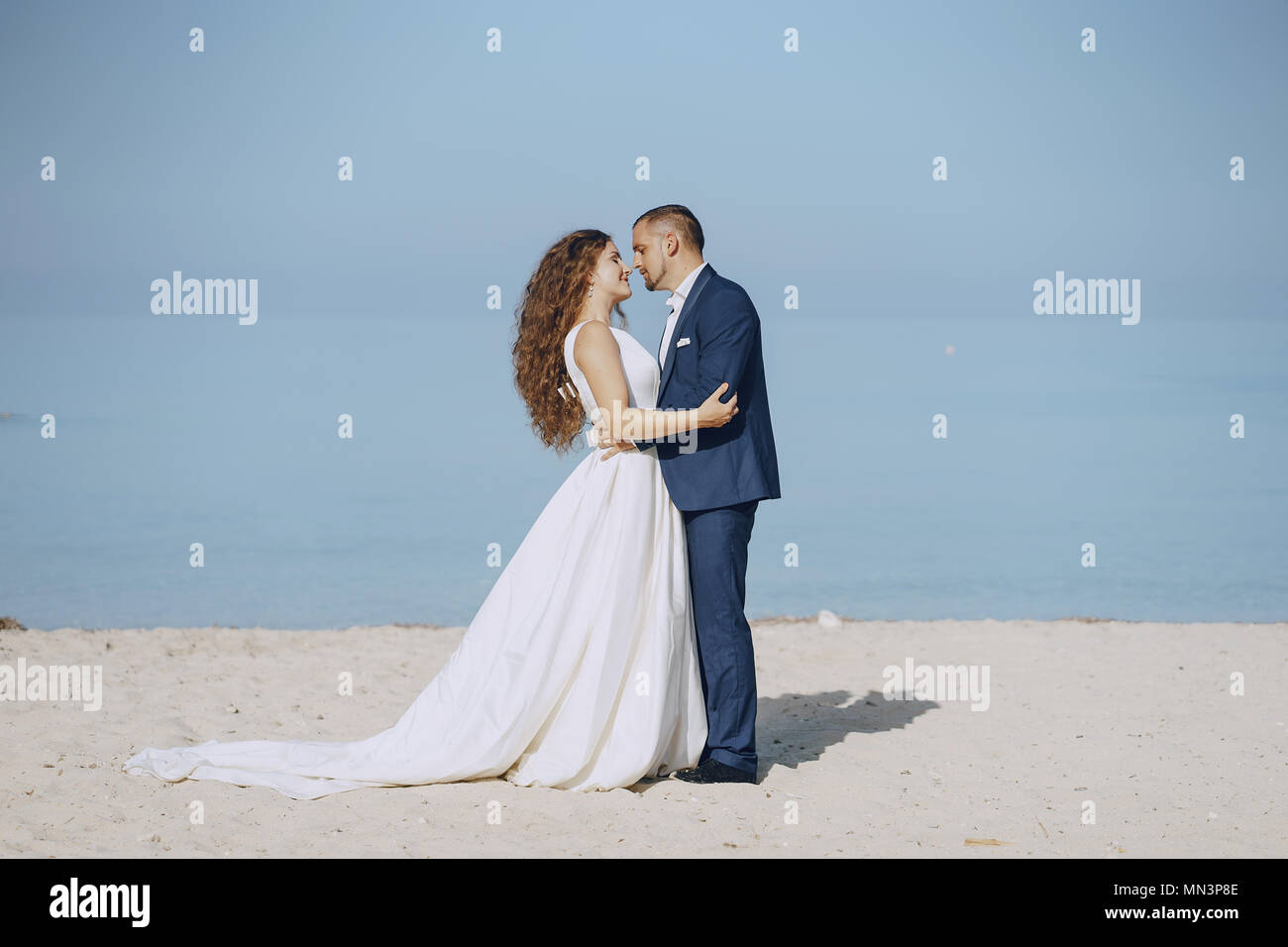 Giovane e bella con i capelli lunghi sposa in abito bianco con il suo giovane marito sulla spiaggia Foto Stock