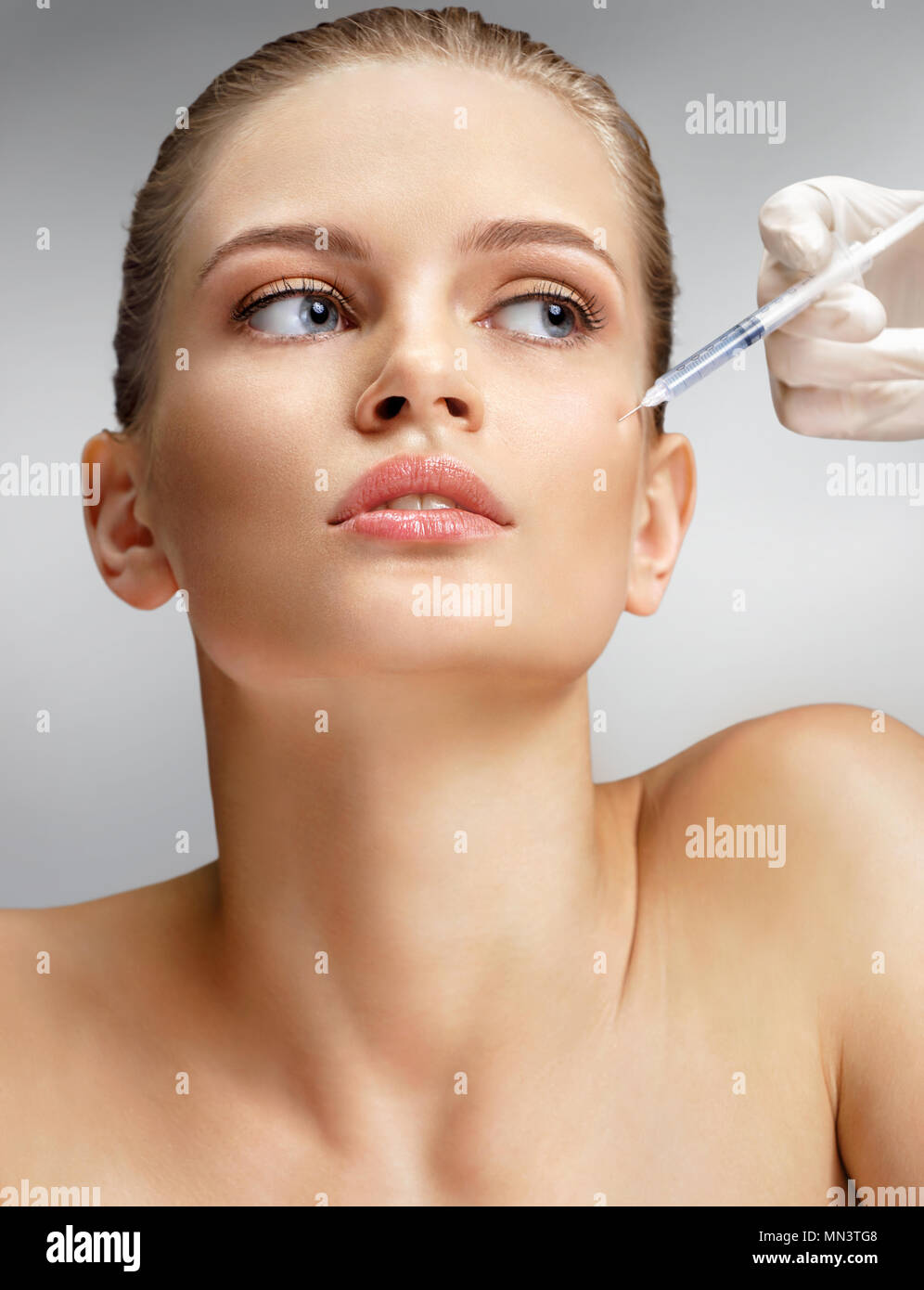 Bella donna di ricezione di iniezione di Botox nella guancia da estetista. Ritratto di giovane donna getting bellezza iniezioni facciali su sfondo grigio. Pulire Foto Stock