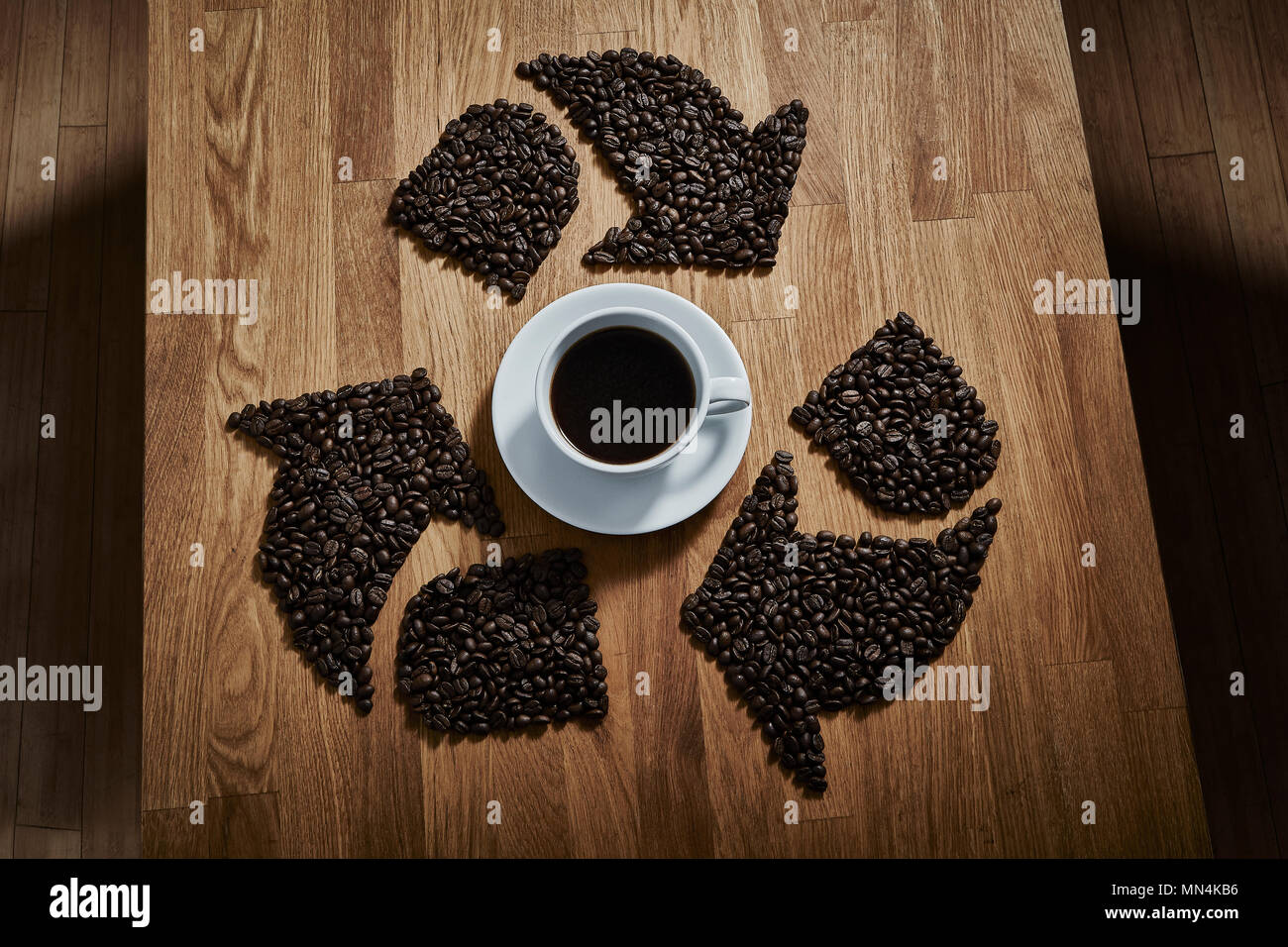 I chicchi di caffè formando simbolo di riciclaggio intorno a tazza da caffè Foto Stock