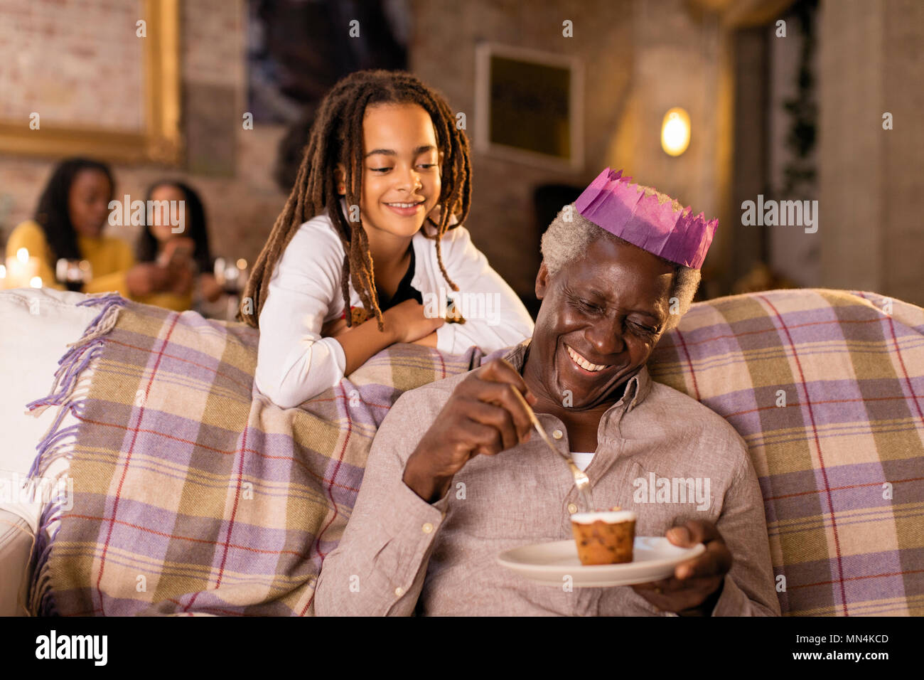 Guardare la nipote nonno in carta di Natale corona di mangiare il dessert Foto Stock