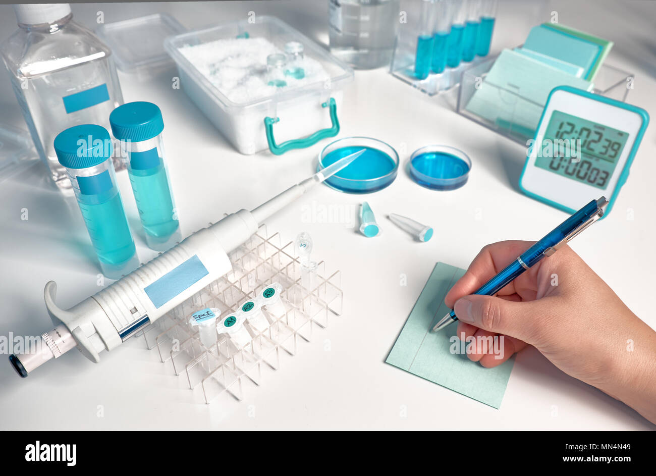 Scientifiche, mediche o di istruzione dello sfondo. Biologico o laboratorio di biochimica fuori fuoco, primo piano sul lato femmina a scrivere una nota. Foto Stock