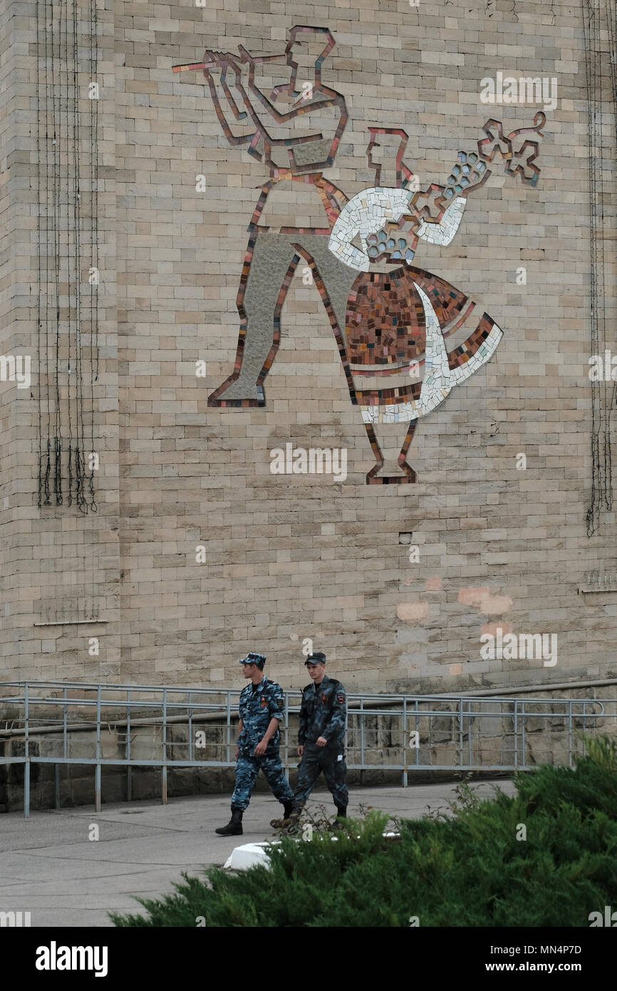 Pridnestrovian guardia di confine di truppe a piedi passato decorazioni sul lato dell era sovietica Casa di Cultura raffigurante una donna che trasportano le uve di un tradizionale simbolo e segno della qualità della Moldavia viticoltura e vinificazione nella città di Bender de facto il nome ufficiale di Tighina all' interno dei confini internazionalmente riconosciuti della Moldavia sotto il controllo de facto della riconosciuta Pridnestrovian Repubblica Moldava anche chiamato Transnistria (PMR) dal 1992. Foto Stock