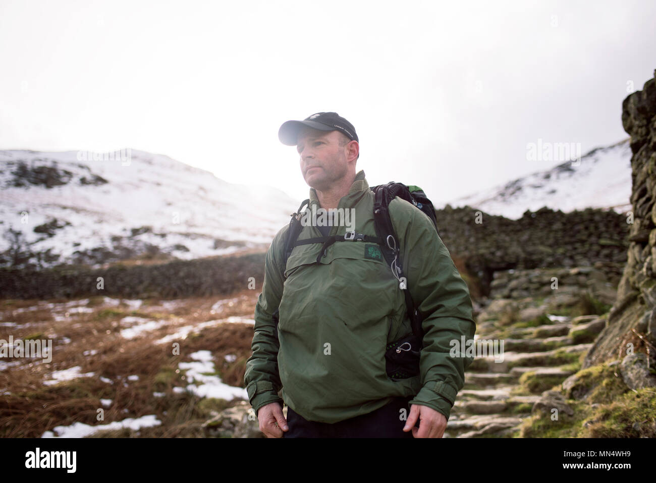Uomo che indossa cappello da baseball escursioni all'aperto. Montagna Innevata del Distretto del Lago, Patterdale, Glenridding, UK. Signor disponibili su richiesta. Feb 2018 Foto Stock