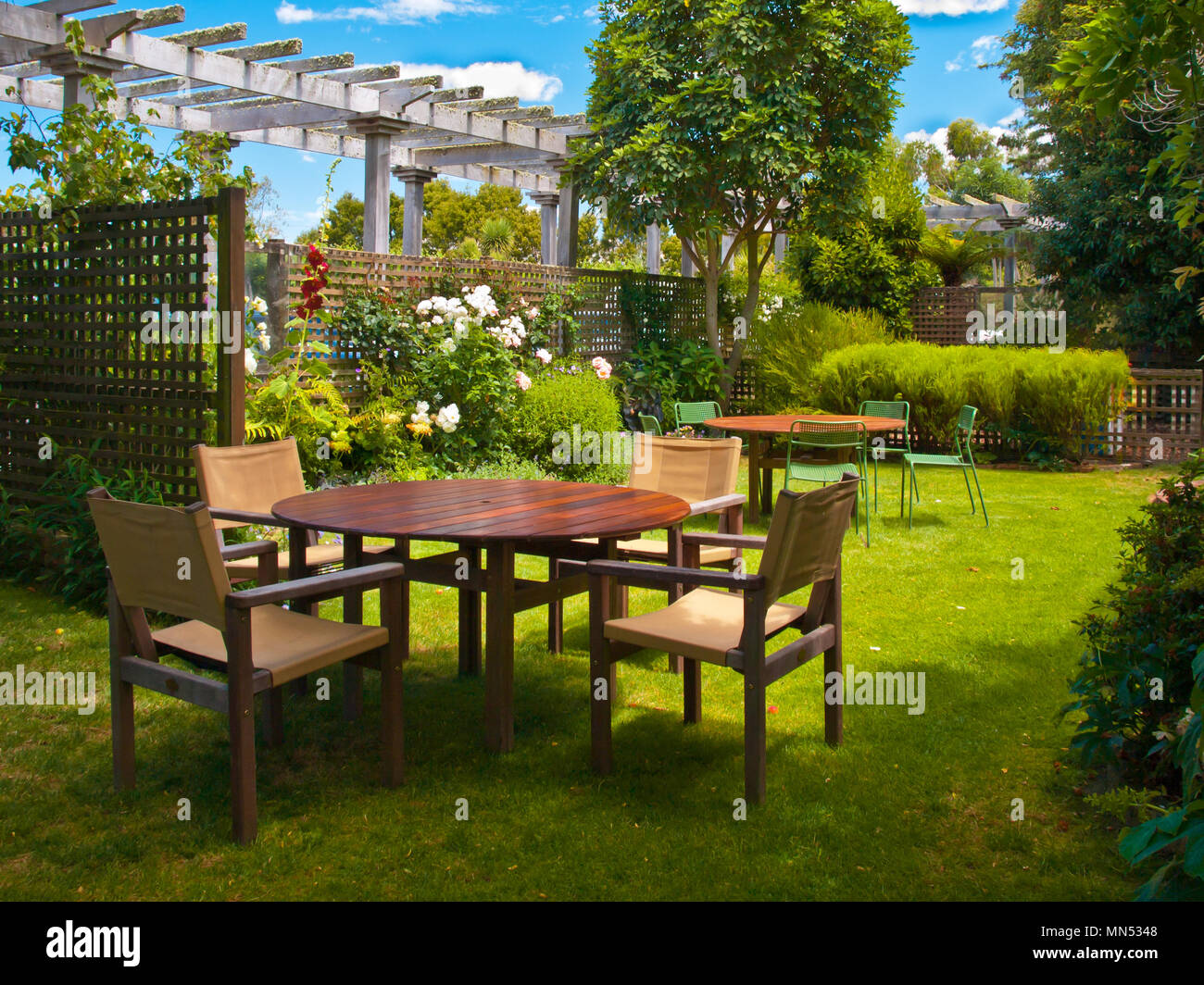 Un paesaggistico giardino con tavolo da pranzo in legno insieme all'ombra di alberi Foto Stock