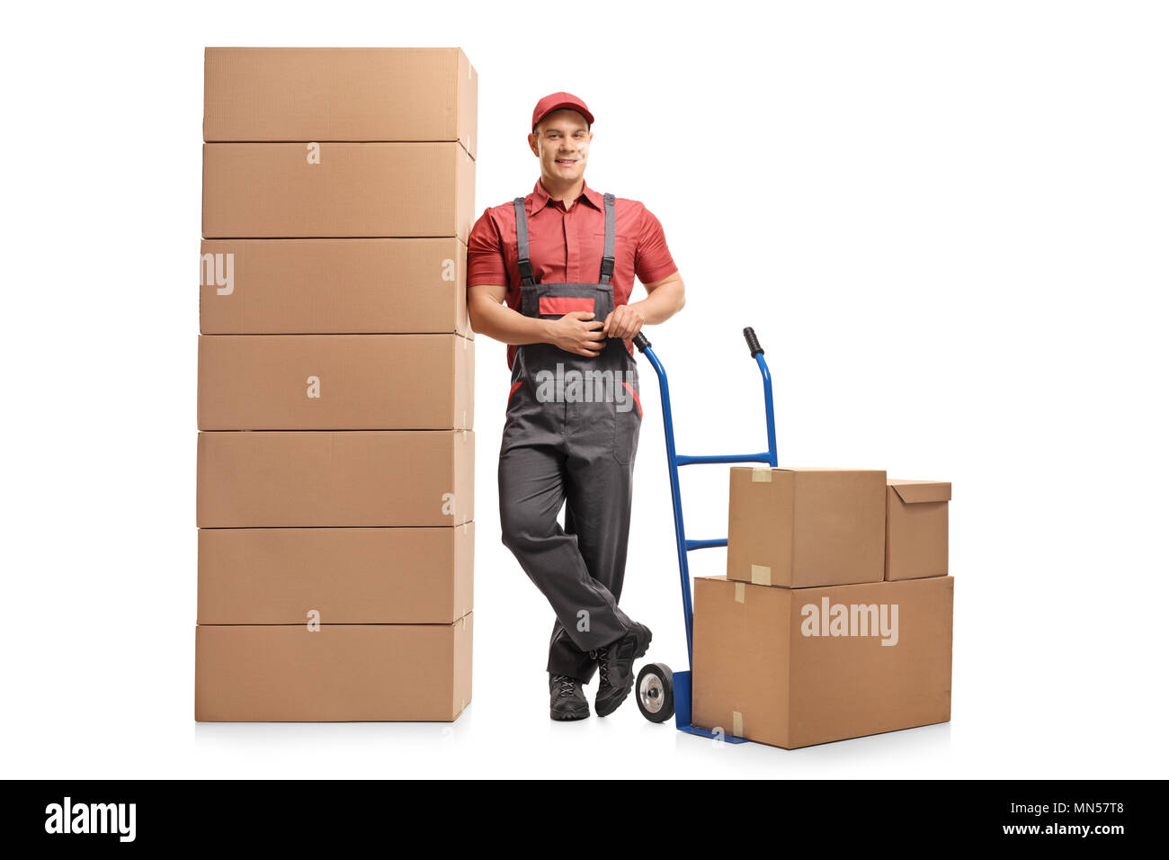 A piena lunghezza Ritratto di un mover con un carrello appoggiato su una pila di scatole e sorridente isolati su sfondo bianco Foto Stock