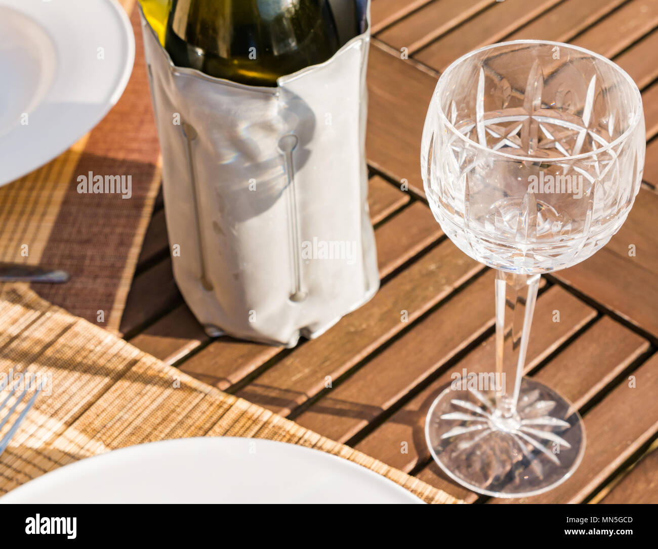 Patio tabella o di una cena o pranzo con le piastre bianche, crostale bicchieri di vino e bottiglia di vino bianco nella luce del sole Foto Stock