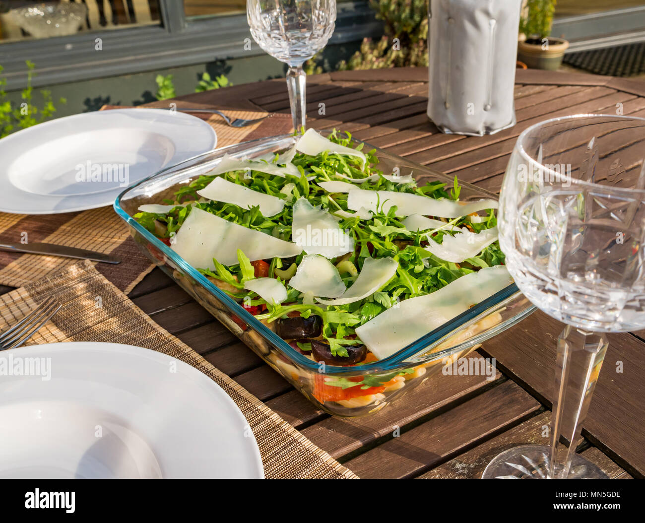 Tavolo esterno nella luce del sole con insalata di pasta piatto, cristallo bicchieri di vino e una bottiglia di vino bianco freddo nello scambiatore di calore Foto Stock