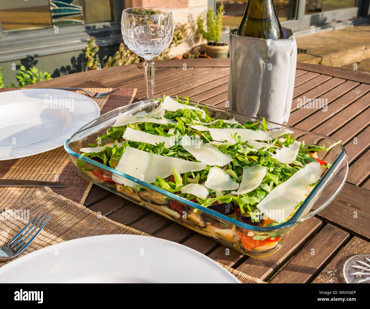 Tavolo esterno nella luce del sole con insalata di pasta piatto, cristallo bicchieri di vino e una bottiglia di vino bianco freddo nello scambiatore di calore Foto Stock