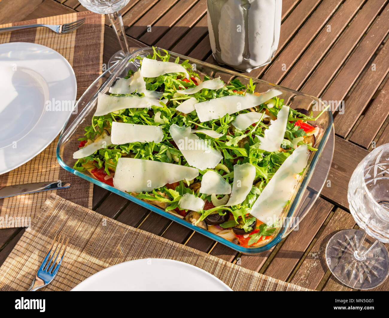 Tavolo esterno nella luce del sole con insalata di pasta piatto, cristallo bicchieri di vino e una bottiglia di vino bianco freddo nello scambiatore di calore Foto Stock
