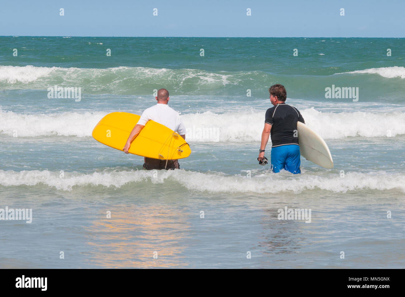 Due maschi a piedi nell'oceano che trasportano le tavole da surf. Preparazione per il surf. Foto Stock