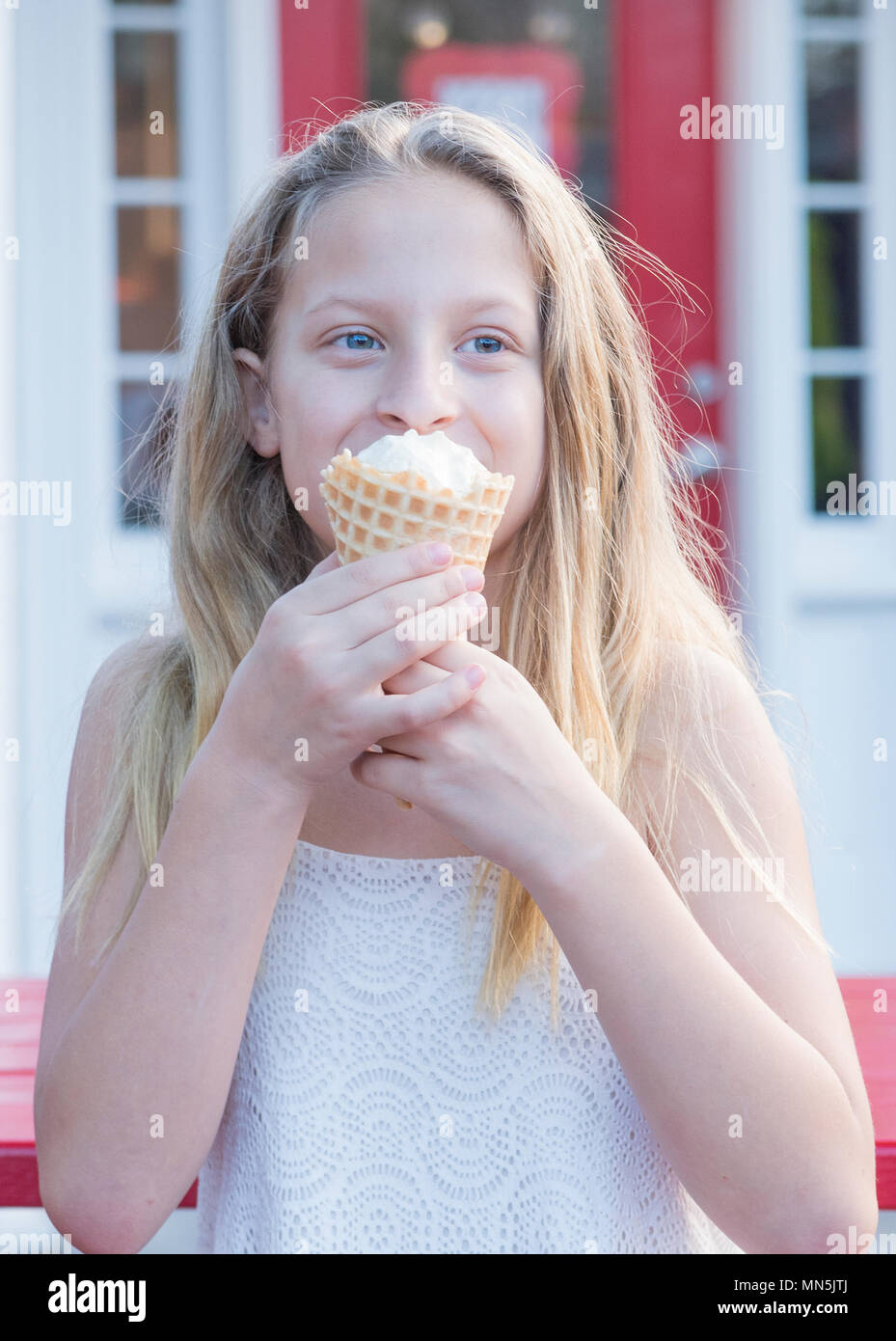 10 anno vecchia ragazza con lunghi capelli biondi godendo di un cono gelato. Immagine viene dalla vita in su. Foto Stock