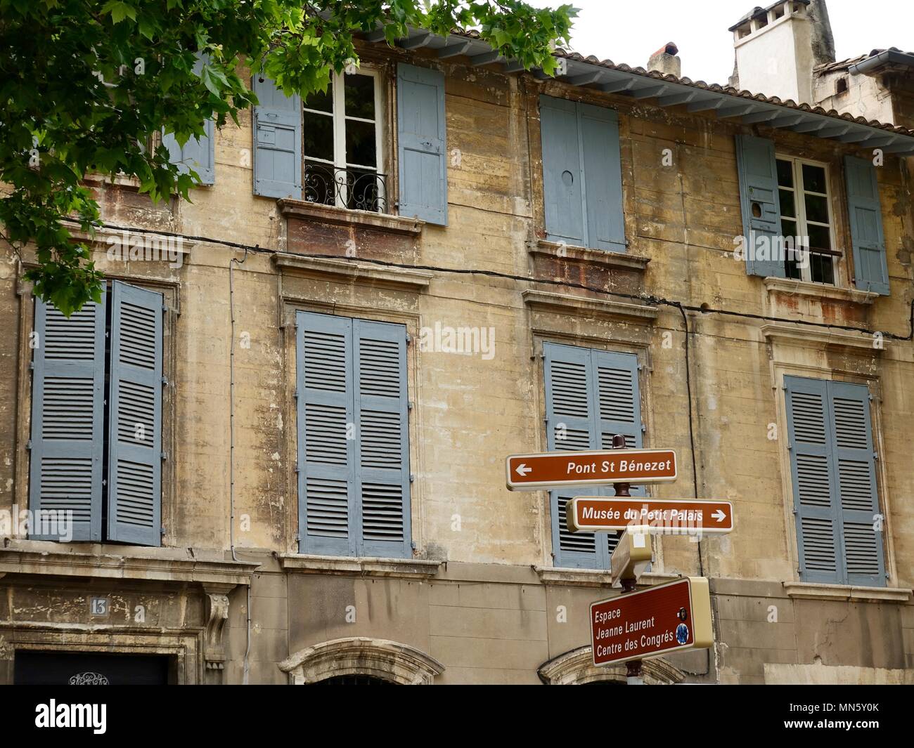 Segnaletica direzionale si trova di fronte a un tradizionale, weathered costruzione in pietra con persiane di colore grigio. Avignon, Francia Foto Stock