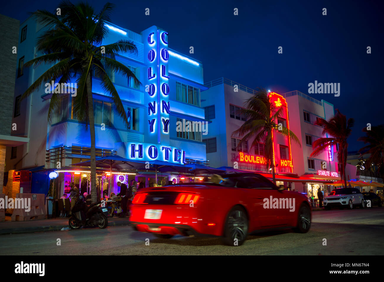 MIAMI - Gennaio 08, 2018: un rosso convertibili rigidi passato iconico hotel art deco e insegne al neon su Ocean Drive in South Beach di notte. Foto Stock