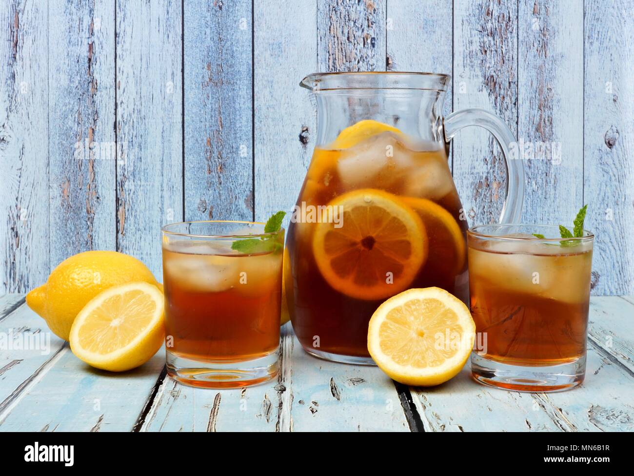Il bricco di tè freddo con due bicchieri e limoni su rustiche blu sullo sfondo di legno Foto Stock