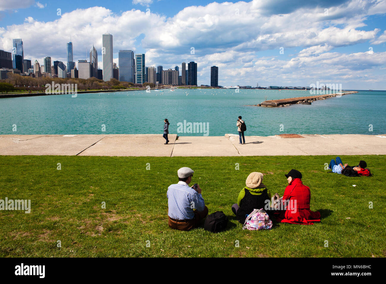 Persone sedersi in un parco lungo il lago Michigan, Chicago, Illinois su un poco nuvoloso cielo blu giorno Foto Stock