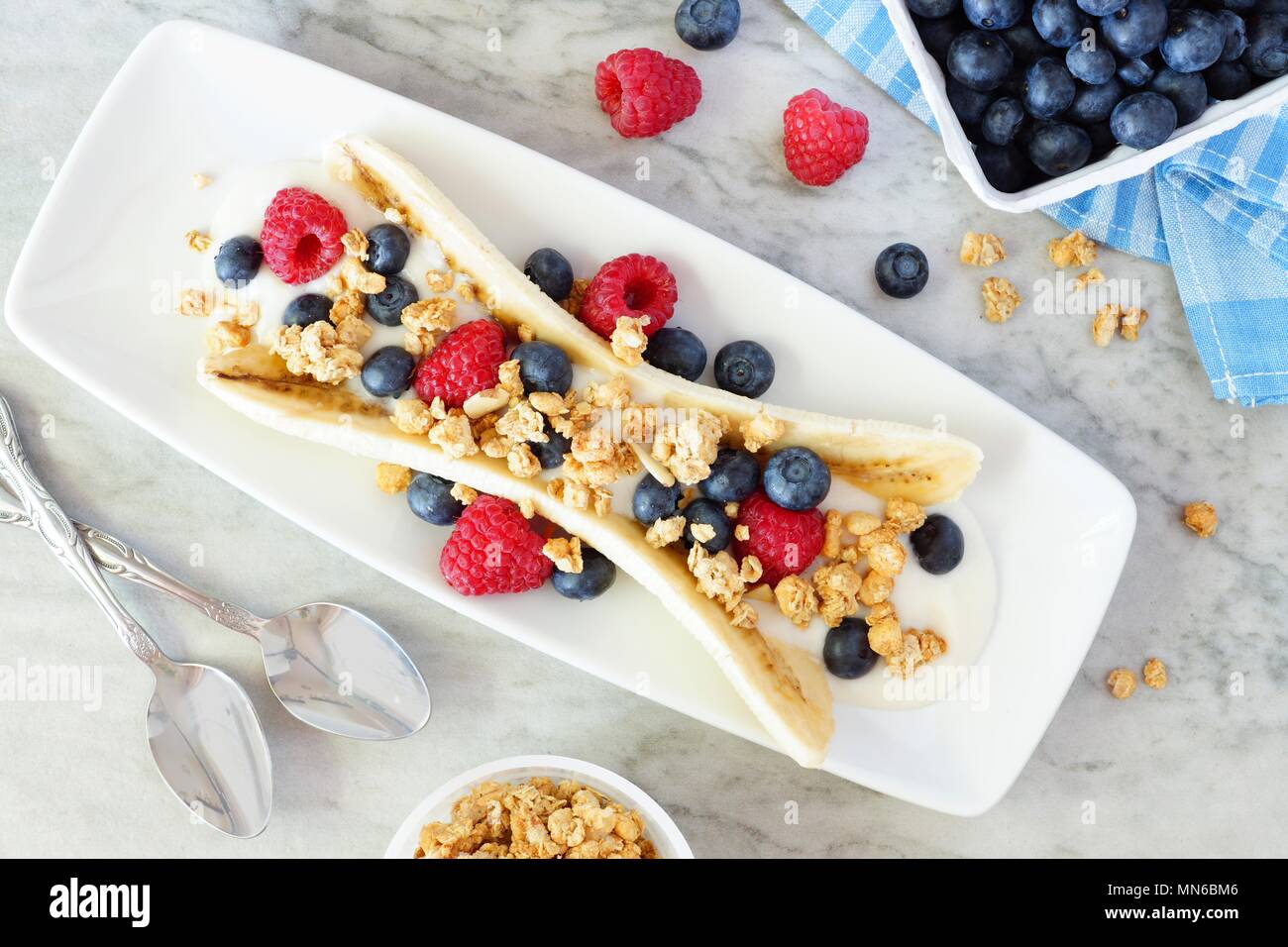 Una sana banana split con yogurt e frutti di bosco freschi e granola, scena di overhead su marmo Foto Stock