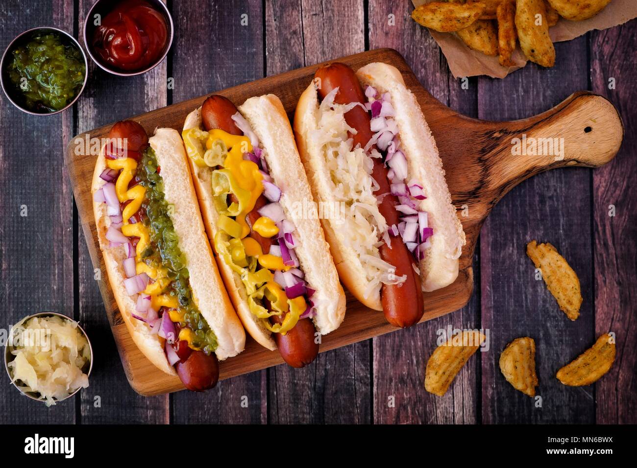 Hot Dogs completamente caricato con farciture assortite su un dispositivo di compressione scheda, scena di overhead Foto Stock