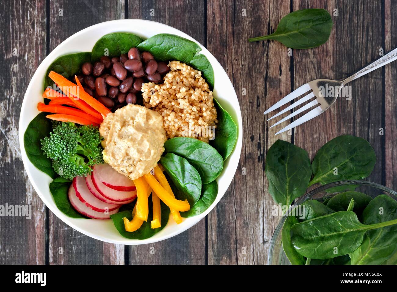 Pranzo sano ciotola con la quinoa, hummus e verdure miste, overhead scena su un rustico sfondo legno Foto Stock