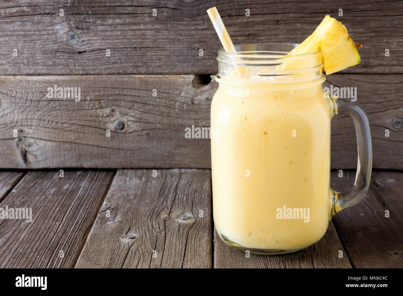 Frullato di ananas in una giara di mason, contro un rustico sfondo di legno Foto Stock