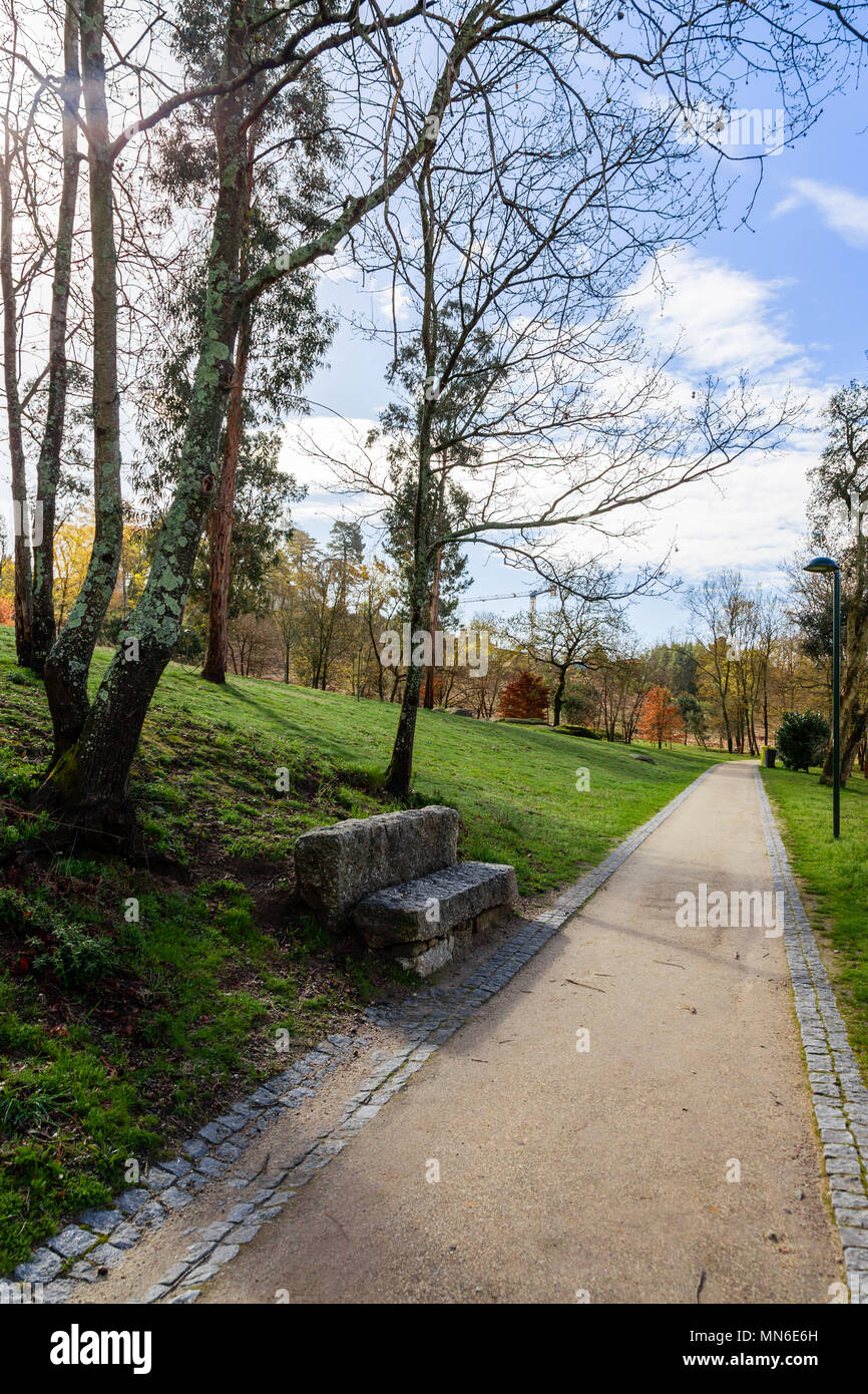 Giardino o una panchina nel parco vicino percorso vuoto, via, sentiero o percorso attraverso gli alberi e il verde prato. Parque da Devesa parco urbano. Vila Nova de Famalicao Foto Stock