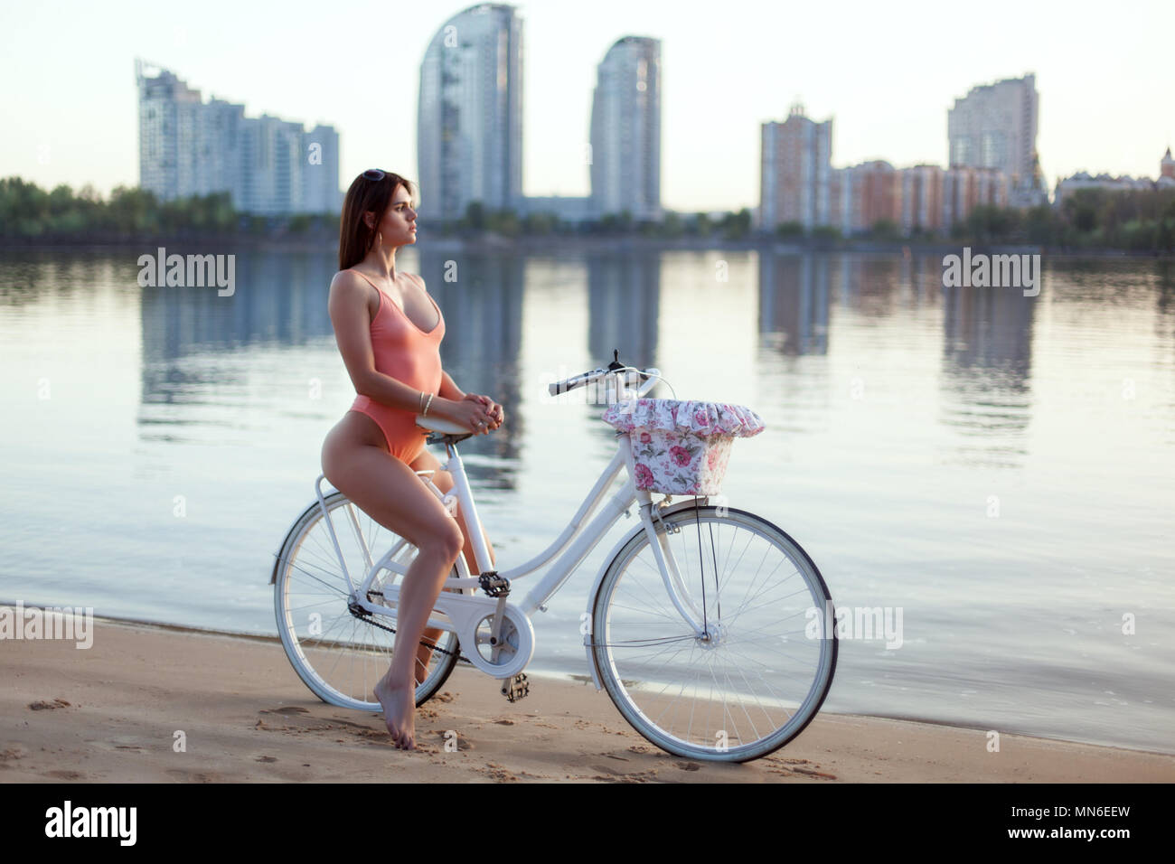 Giovane donna in costume da bagno si siede su una bicicletta sulla riva del fiume. Foto Stock
