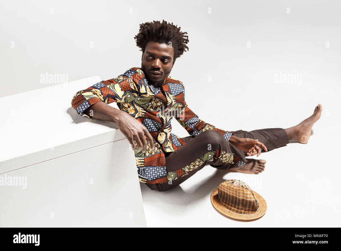 Vista da abow giovane adulto uomo afro, seduto sul pavimento . Indoor, isolata su uno sfondo grigio Foto Stock