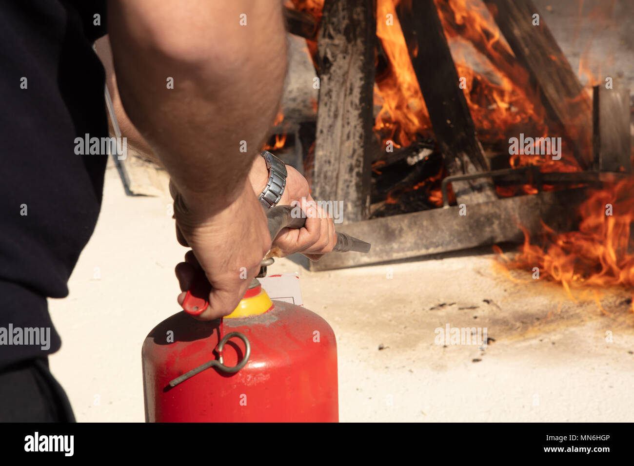Giovane uomo rivolto in rosso di un estintore in avanti verso il fuoco in una situazione grave Foto Stock