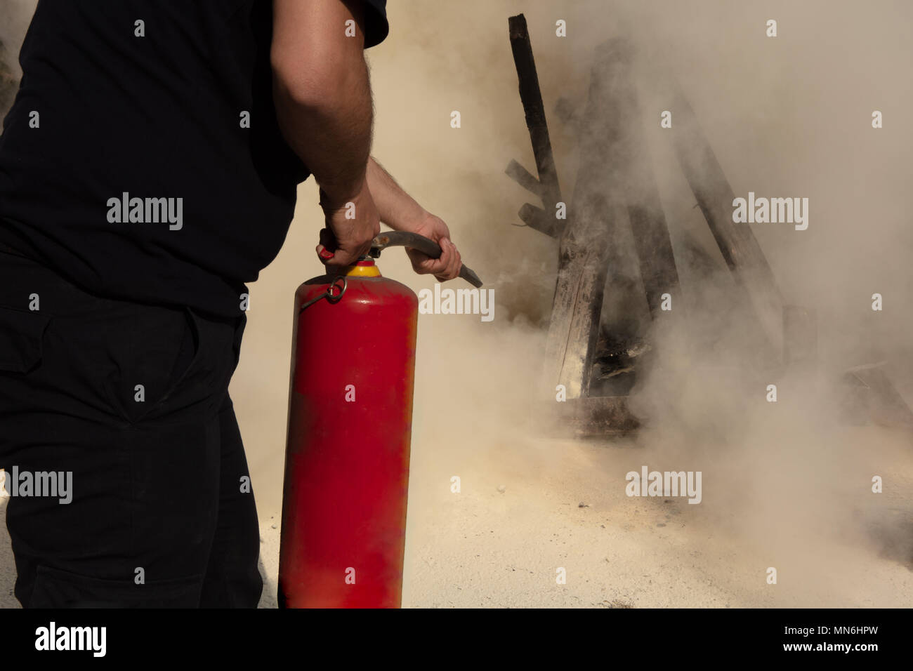 Giovane uomo puntando il tipo in polvere di estintore in avanti verso il fuoco in una situazione grave Foto Stock