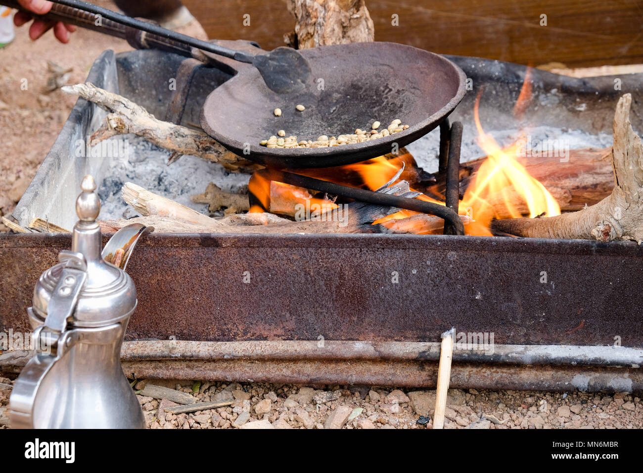 I chicchi di caffè essendo rosted sul fuoco accanto a un tradizionale caffè beduino pentola o dallah Foto Stock