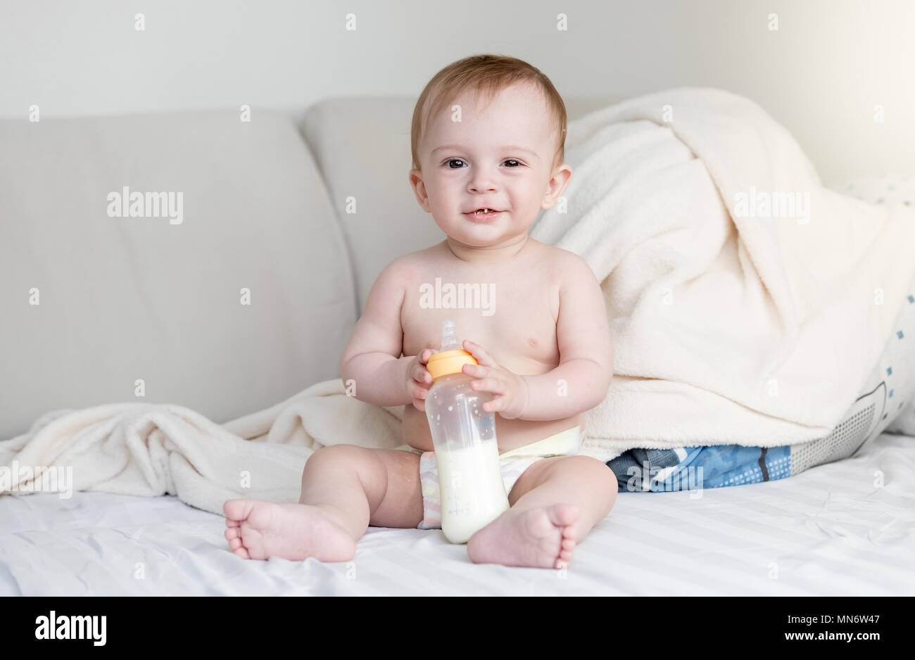 Ritratto di carino sorridente bambino seduto sul letto e tenendo la bottiglia di latte Foto Stock