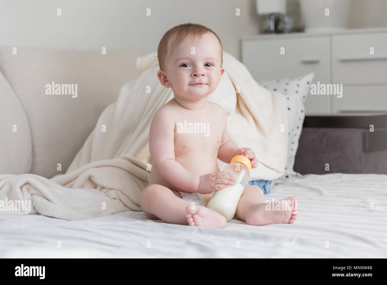 Carino 9 mesi baby boy in pannolini seduta con bottiglia di latte sul letto Foto Stock