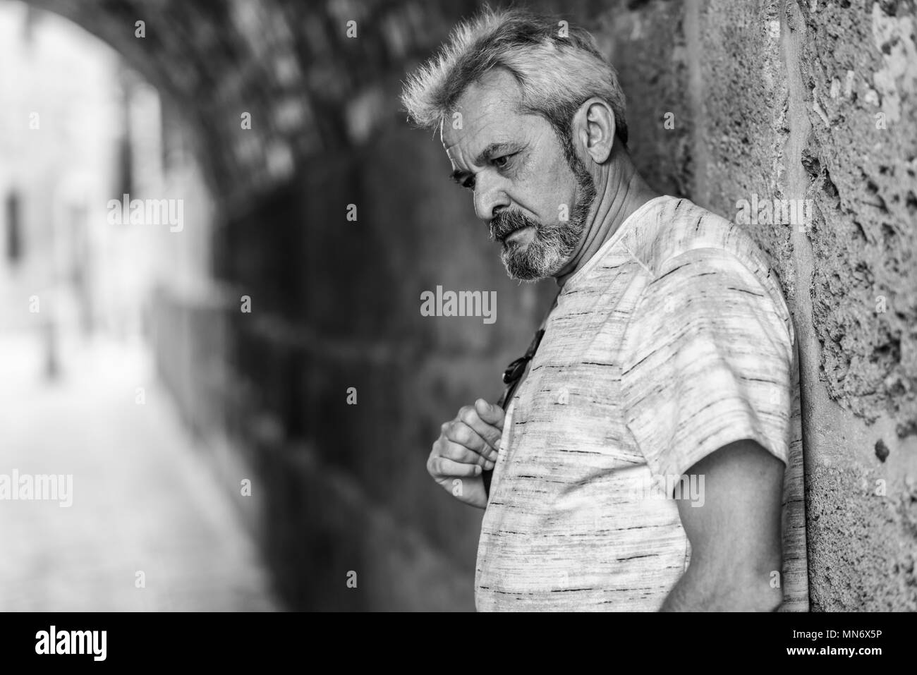 Ritratto di un uomo maturo con i capelli grigi in background urbano. Senior maschio con i capelli bianchi e la barba di indossare un abbigliamento informale. Foto Stock