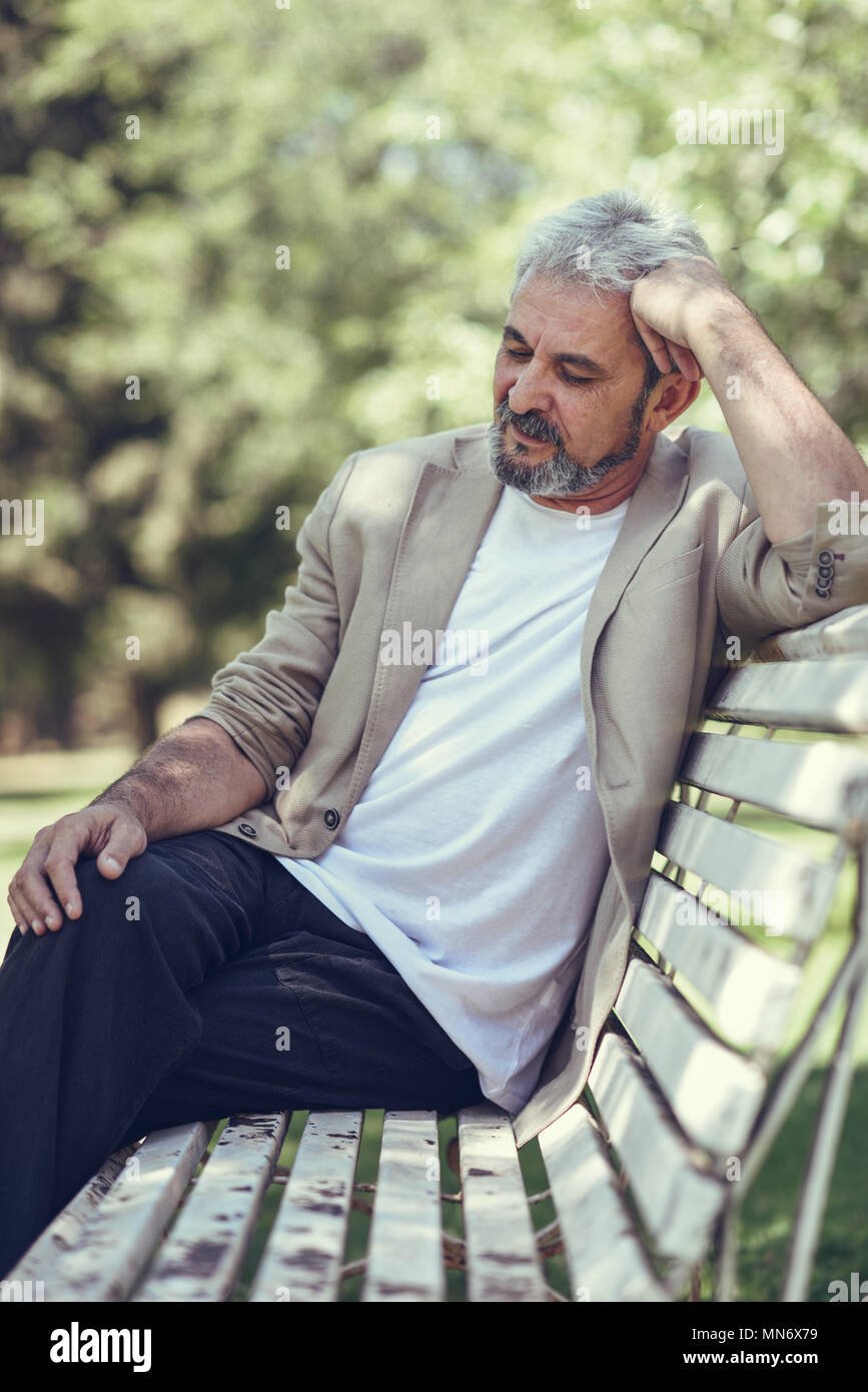 Ritratto di un pensieroso uomo maturo seduta su una panchina in un parco  urbano. Senior maschio con i capelli bianchi e la barba sorridente  indossando un abbigliamento informale Foto stock - Alamy