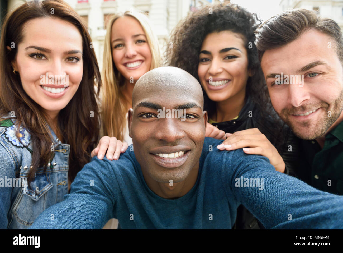 Gruppo multirazziale di amici prendendo selfie in una strada urbana con un uomo nero in primo piano. Tre giovani donne e due uomini che indossano un abbigliamento informale. Foto Stock