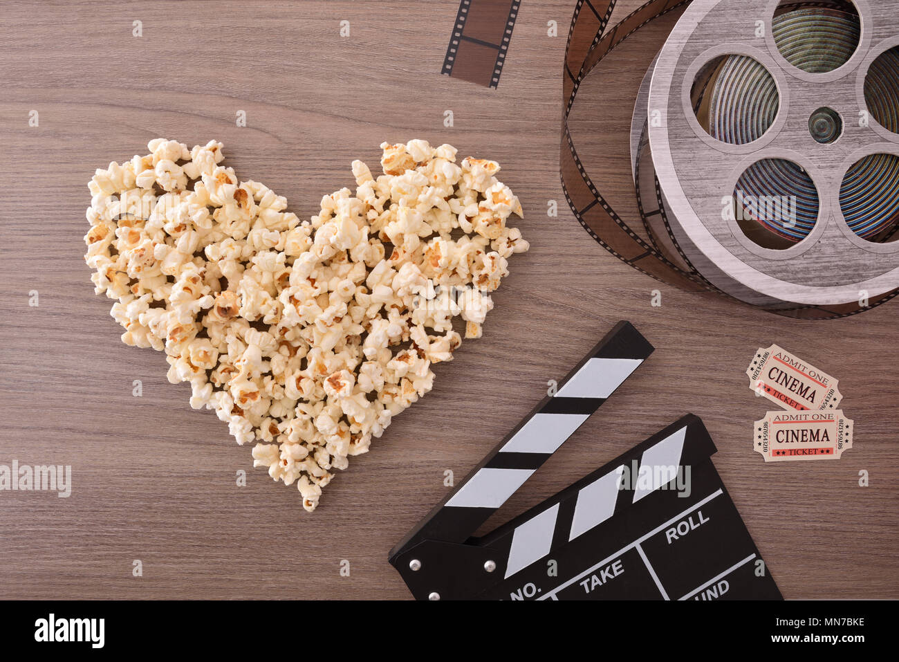 Le attrezzature e gli elementi del cinema sul tavolo di legno con popcorn cuore. Concetto di guardare film. Composizione verticale. Vista dall'alto. Foto Stock